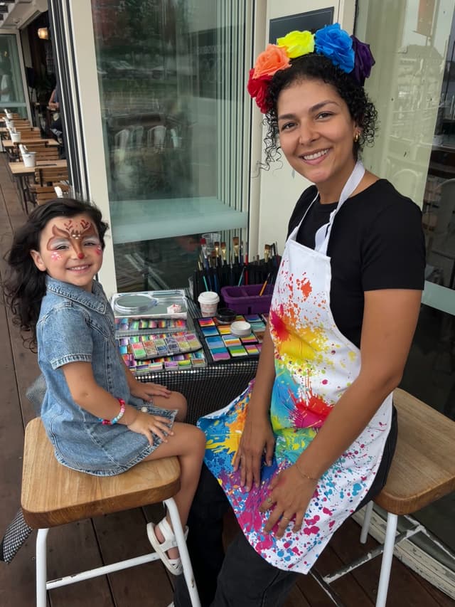 Nadia with rainbow apron painting a happy child